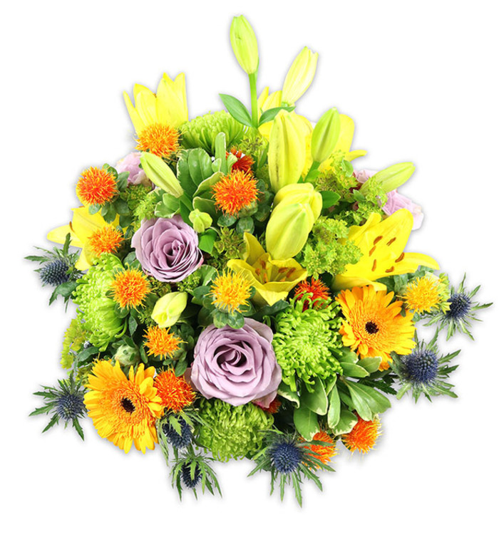 A richly coloured, professionally composed floral mound rests against pristine white, each bloom chosen to harmonise colour, scent and form with confident artistry often practised by florists working around Mitcham Junction and the town centre. Dominant yellow Asiatic lilies create the vertical structure: several are fully unfurled with freckled inner petals and visible pollen-bearing stamens, while others remain elongated buds that promise unfurling. Two or three soft lavender roses anchor the centre, their velvety spirals offering a calm, romantic counterpoint to the energetic oranges. Bright orange Gerbera daisies, with their broad, flat petals and darker centres, read like cheerful suns throughout the design, and lime-green button chrysanthemums supply dense, ruffled texture that fills negative space and gives the arrangement a lush, almost mossy presence. Interspersed are small spherical orange and yellow accent blooms-reminiscent of Billy Buttons or craspedia-that add whimsical punctuation and tactile variety. Several blue-grey Eryngium thistles extend from the sides and lower edges, their starry bracts and sharp silhouettes delivering a cool, architectural riff against the warm palette. Various greens-broad lily leaves, glossy fillers and delicate sprigs-frame and unify the flowers, creating depth and movement under soft, even lighting. The overall impression is versatile and emotive: celebratory without excess, comforting without being austere, perfect for a birthday table, an anniversary, or a thoughtful message of sympathy delivered from a local hand in Mitcham.
