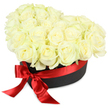 Elegance and heartfelt sentiment abound in this Mitcham-inspired heart-shaped hatbox, overflowing with dozens of hand-selected white roses. Each blossom is meticulously arranged to create a plush, inviting mound-petals of pure ivory mingling with hints of green at the base, suggesting their garden-fresh quality. The contemporary matte black box provides a striking frame, its understated style echoing the modern tastes of Mitcham residents and offering a beautiful contrast to the radiant blooms. Around the base, a luminous scarlet red satin ribbon wraps gracefully, tied into an exuberant bow whose flowing ends add drama and a loving touch. The arrangement's gentle, even lighting enhances every soft curve, shadow, and highlight, setting it apart against a clean white background. This sophisticated ensemble is perfect for delivering love on anniversaries, celebrating new beginnings, or offering a gentle gesture of remembrance-serving as a thoughtful gift for any occasion throughout Mitcham, from the vibrant markets near London Road to quiet family gatherings. The lush scent of fresh roses completes the sensory experience, capturing the essence of luxury and personal devotion that defines flower delivery in the Mitcham community.